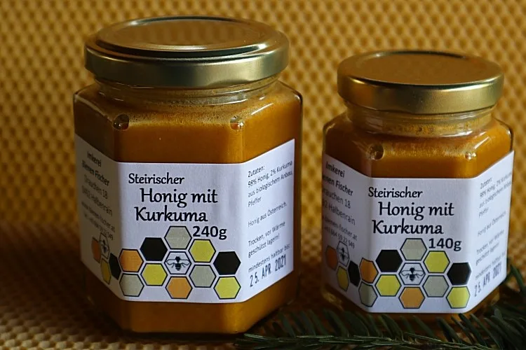 Zwei Gläser Steirischer Honig mit Kurkuma in den Größen 240g und 140g auf einer Wabenplatte
