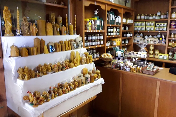 Stufenregal im Hofladen mit Figuren und Kerzen aus Bienenwachs, dahinter die Regale mit Honiggläsern
